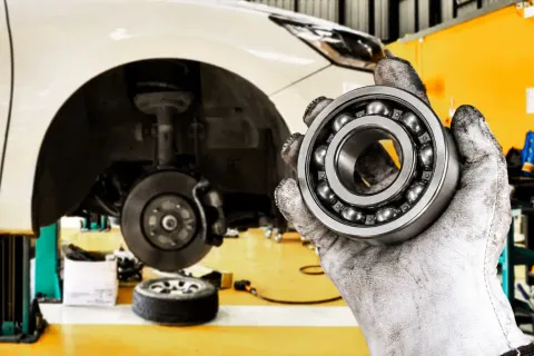 Wheel bearing replacement service showing a technician holding a new wheel bearing next to a vehicle with the wheel removed.