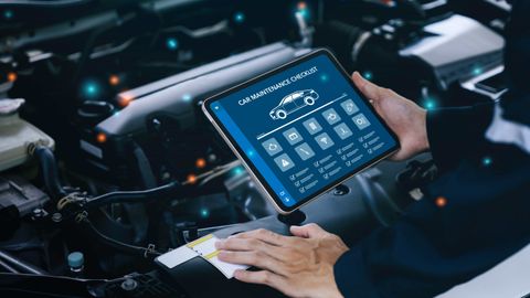 Professional automotive technician performing a digital vehicle inspection under the hood of a modern vehicle inside a clean Phoenix auto repair shop, using a tablet inspection checklist with Arizona sunlight visible in the background.